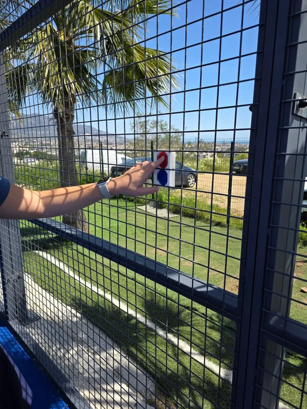 Close-up of the red LedsCount Pro RF remote clipped to a padel court fence.
