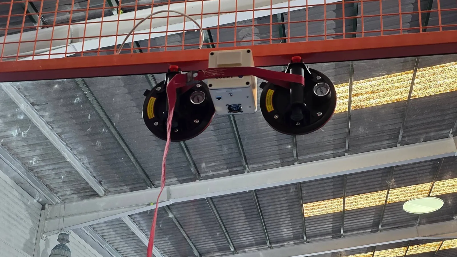 Installation in progress — heavy-duty suction clamps holding the camera enclosure against the court glass while industrial-grade 3M VHB adhesive cures.